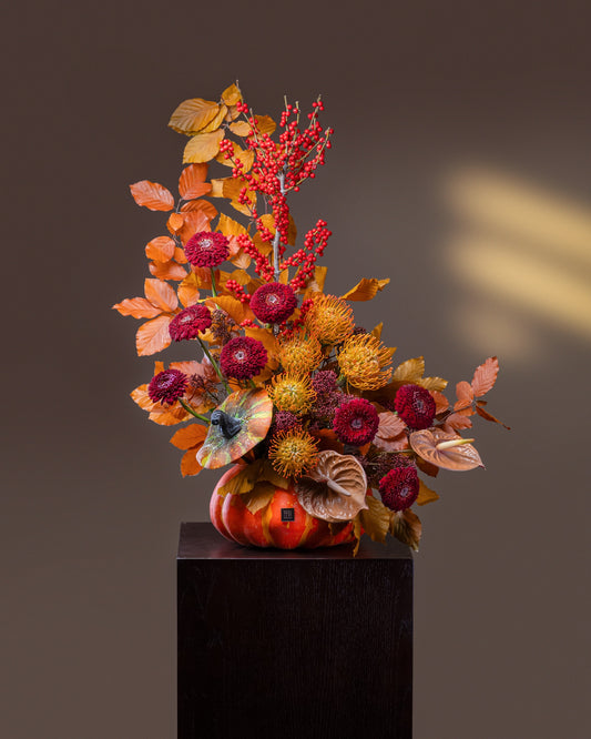 Bewitched Pumpkin Flower Arrangement luxury Halloween floral design in an heirloom pumpkin with red ilex berries, golden pincushion proteas, and crimson blooms