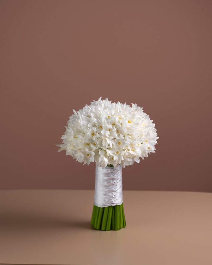Bouquet of white flowers in a green vase on a beige surface with a brown background