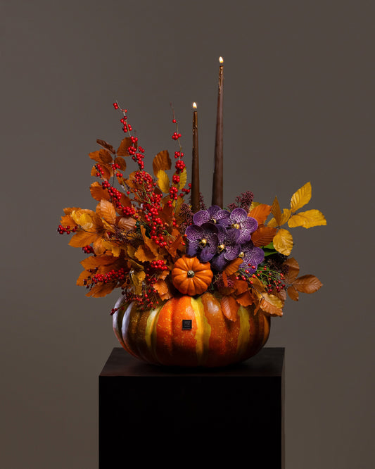Spooky Pumpkin Flower Arrangement featuring purple Vanda orchids, red ilex berries, and glowing brown taper candles in a carved pumpkin
