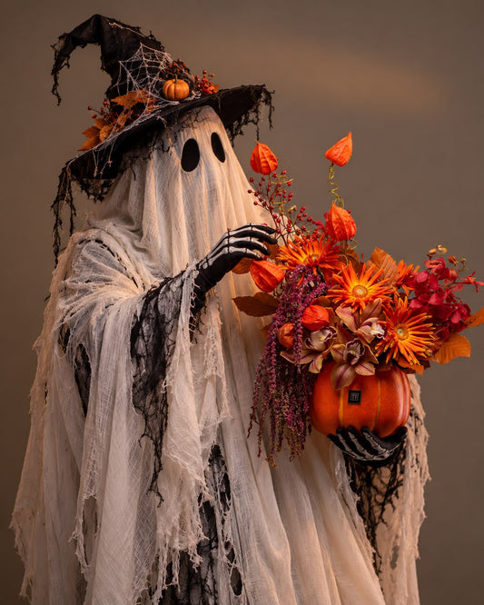 Twilight Pumpkin Flower Arrangement featuring fiery autumn floral blooms and floating lantern accents in an orange ceramic pumpkin vase on a pedestal