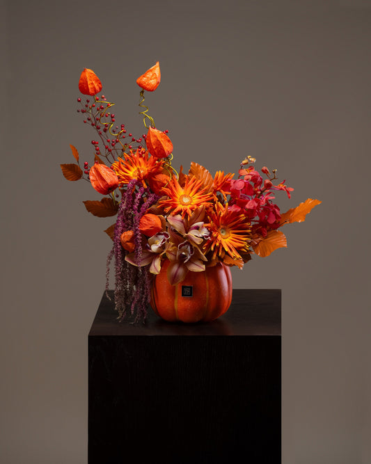 Twilight Pumpkin Flower Arrangement featuring fiery autumn floral blooms and floating lantern accents in an orange ceramic pumpkin vase on a pedestal